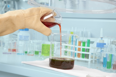 A protected Chemist is decanting an acidly red liquid into an already filled beaker の写真素材