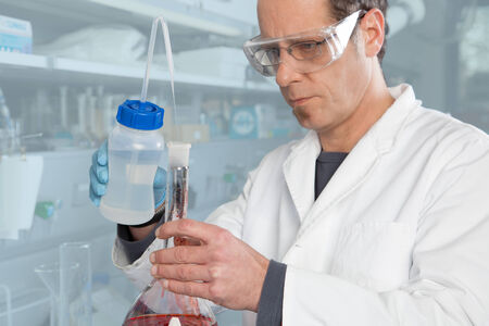 A Chemist is mixing two liquids in a glass container の写真素材