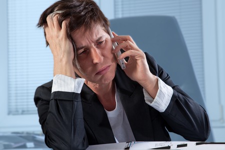 A woman is a step before to break out in tears during a phone call in her office の写真素材