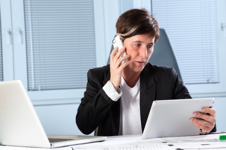 A secretary is using a phone, mobile device and a personal computer at the same time for the business の写真素材