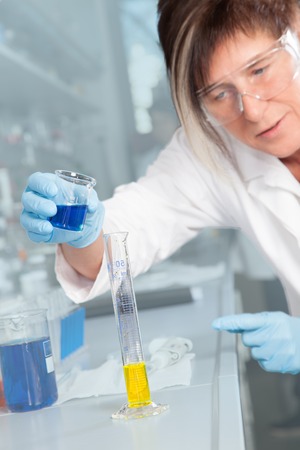 The Laboratory Assistant is decanting a blue liquid into a Test Tube with a yellow Liquid の写真素材