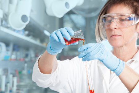 A Chemist is decanting a red Liquid into a large test tube の写真素材