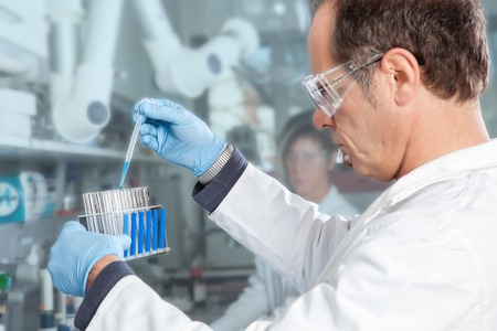 A Professor extracts a blue Liquid probe from a filled test tube の写真素材