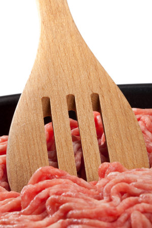 A piece of raw minced meat with a wooden spoon in a pan 