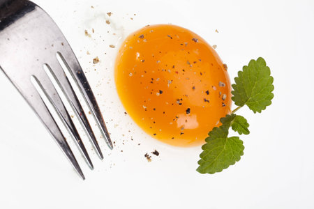 A fork is picking into a raw egg decorated with some basil の写真素材