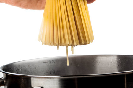 A woman is holding some pasta over a pan with hot water の写真素材
