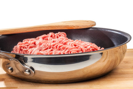 A side view from a filled pan with minced meat and a wooden spoon on top の写真素材