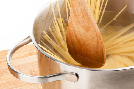 A wooden spoon is stirring some pasta in a pan which is filled with hot water の写真素材