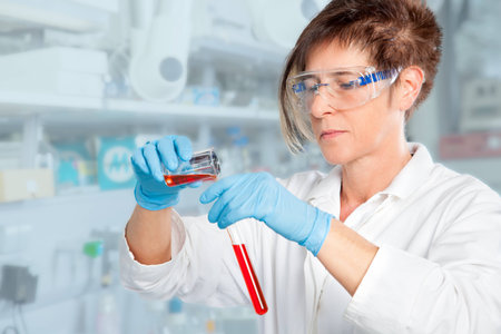 A Chemist student is decanting a red liquid into a test tube in her laboratory の写真素材