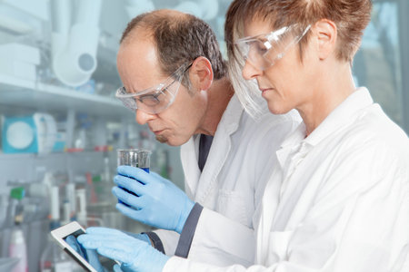A Doctor smells a liquid while the assistant is entering the result into a mobile device の写真素材