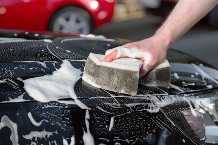 A man is washing his black car with a sponge.の写真素材
