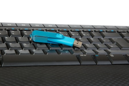 A blue USB Stick lying on a black Keyboard isolated on white.の写真素材