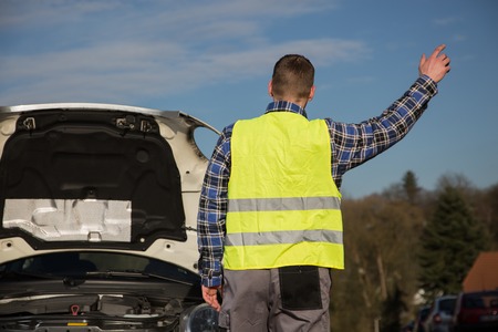 A young man asks for help on the road near his broken carの写真素材