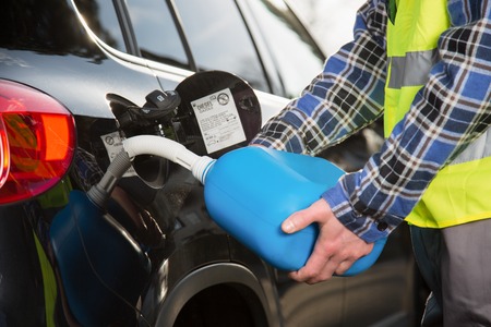 A young man is refueling a vehicle with a blue plastic canister.の写真素材