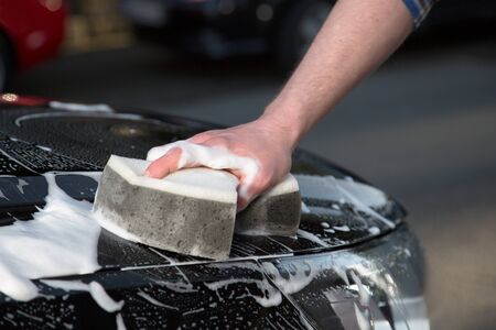 A man is washing his car with a sponge on the road.の写真素材