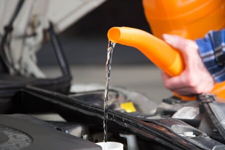 A man is filling fresh water into the canister of the car windscreen wiper system.の写真素材