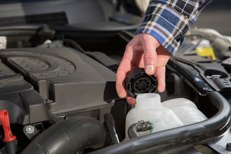 A service mechanic opened the cap from a car water canister to inspect the water level for the engine.の写真素材