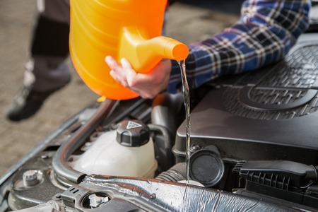 A man is filling the car water cooling system with fresh water from an orange canister.の写真素材