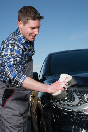 A man is cleaning a car on the street with a sponge and foam.の写真素材
