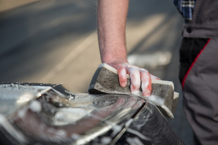 A man is cleaning a car engine hood with a sponge.の写真素材