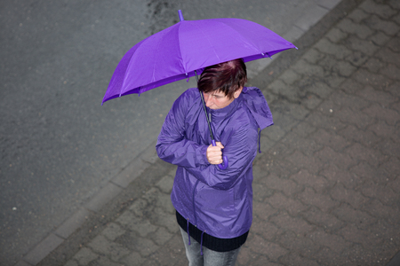 A raincoat dressed woman is standing in the rain and is freezing.の写真素材