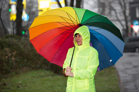 A rain protected woman waiting in the rain with her colorful umbrella.の写真素材