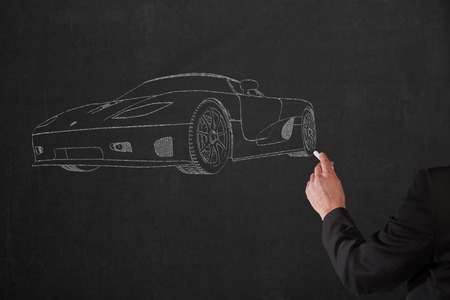 A Businessman is drawing a sportscar on a black used chalkboard by hand.の写真素材