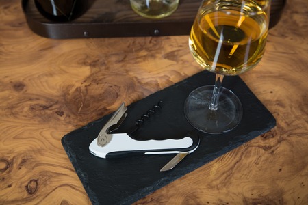A vine bottle opener on a roof slate with a glass of white wine.の写真素材