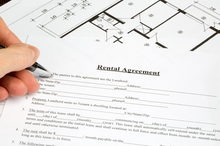 A human hand is filling out a Rental Agreement document. A Floor plan is lying beside the Agreement document.の写真素材
