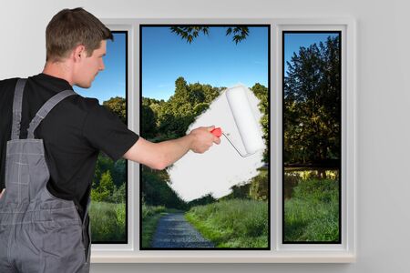 A young man is painting a window with a white color.の写真素材