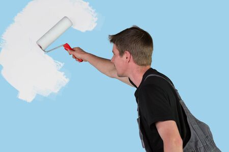 A young man is repainting the turquois wall with a new white tint.の写真素材