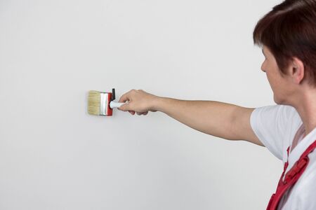 A woman is painting a grey wall with a paint brush. A lot of copyspace available.の写真素材