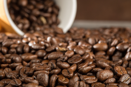 A bunch of coffee beans with a cup of beans in the background.の写真素材