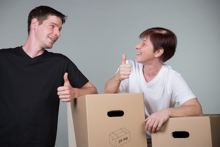 A couple standing beside some cardboards with thumbs up isolated on grey.の写真素材