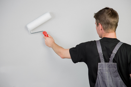 A young man finished the wall painting with a roller. Man in back view is isolated on a grey background.の写真素材
