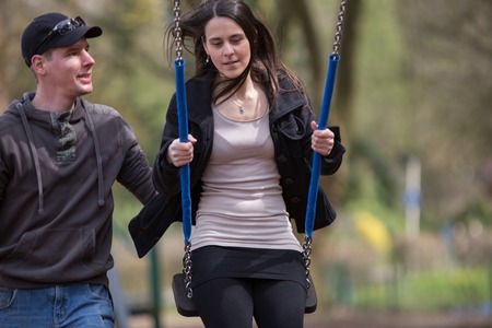 A young couple is using a swing at a playgound.の写真素材