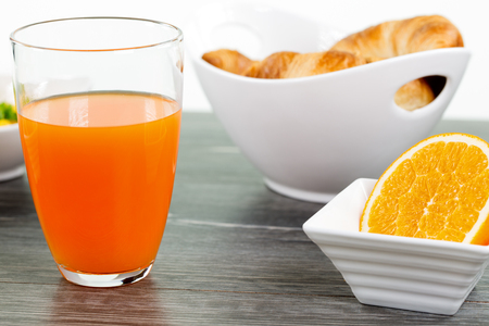 A glass of orange juice with a sliced orange fruit in a bowl on a wooden table. Some Bread in a bowl in the background.の写真素材