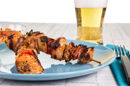 Two shashlik spits on a bluish plate, decorated with a beer in the background.の写真素材