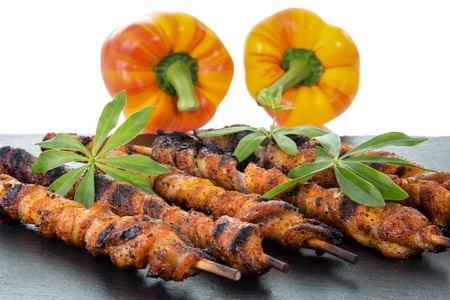 A couple of wrapped meat spits on a slate decorated with two paprika, isolated on white with copyspace.の写真素材
