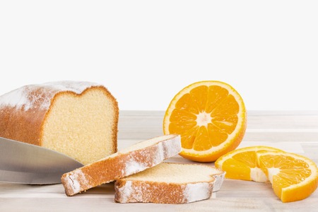 A knife is cutting a lemon cake with some orange fruits on a wooden table. Isolated on a white background.の写真素材