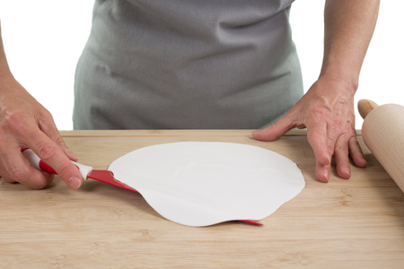 A woman cook lifts the dough with a big knife from the wooden board, isolated on a white background.の写真素材