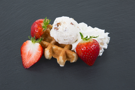A round waffle decorated with ice, strawberry and cream laying on a dark slate with copyspace.の写真素材