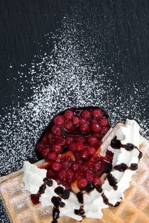 A top view from waffles with cream and cranberries decorated with chocolate stripes on a dark slate with powdered sugar.の写真素材