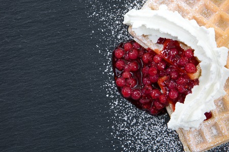 A top view from waffles with cream and cranberries on a dark slate with powdered sugar and copyspace.の写真素材