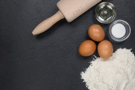 A top view form some ingredients and a rolling pin for cookie baking on a dark slate.の写真素材
