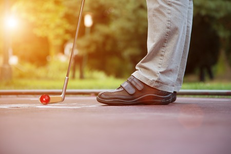 A minigolf player tries to put a ball into the hole at a sunny day with lens flares.の写真素材