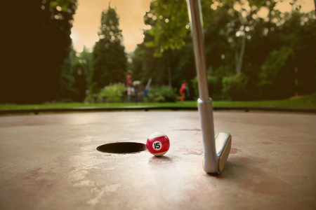 A minigolf player tries to put a small billard ball into the hole with his iron racket.の写真素材