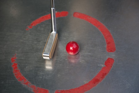 A red minigolf ball with an iron racket at the minigolf playground with visible reflections at the ground.の写真素材
