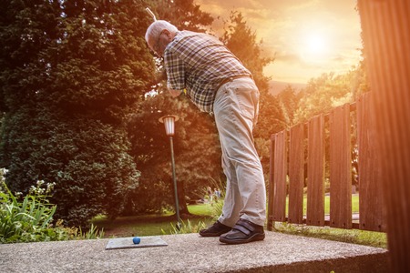 A male senior at minigolf game. He strikes out to push the ball in the right direction.の写真素材