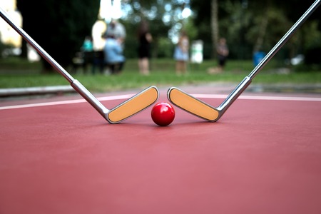 Two minigolf iron rackets and a red ball at a court ground.の写真素材